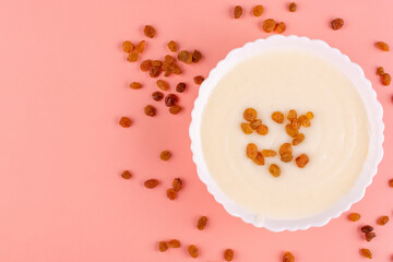 Semolina porridge with raisins in a beautiful white plate (bowl) on a peach-pink background. Place for text, recipe. Contains gluten.