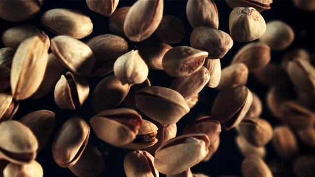 Pistachios rise up and rotate in flight. Top view. On a black background. Filmed is slow motion 1000 fps.