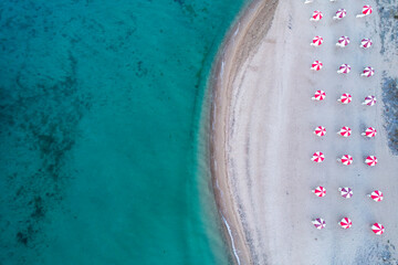 Aerial view of sea. Empty sandy beach with sun beds and umbrellas at sunny day in summer. Tropical landscape with clear turquoise water, deck chair.