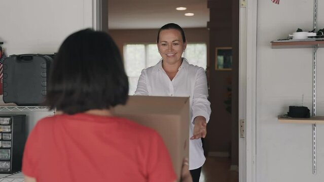 Beautiful and Smiling Woman Receives a Large Cardboard Box from Deliver Driver on the Doorstep with Open Doorway of Her Home. Slow Motion. Shipping and Delivery Concept