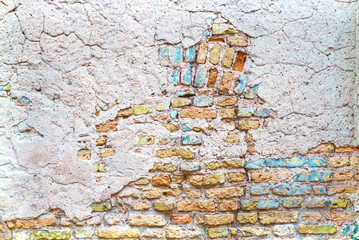 Old brick wall with patches of blue and yellow plaster paint