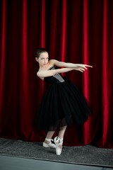 A cute ballerina girl in a black dress on a red background. Art. Dance. Beauty.