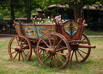 Fototapeta na wymiar Old primitive painted wooden cart with large wooden spoke wheels holding blooming plants and flowers as seen in Veliko Tarnovo, Bulgaria..