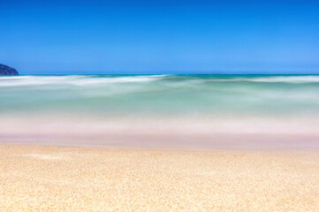 Fototapeta na wymiar Langzeitbelichtung eines Sandstrandes mit türkisblauem Meer vor blauem Himmel