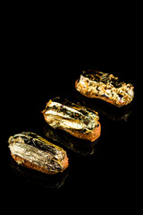 Eclair on a black background decorated with edible gold.