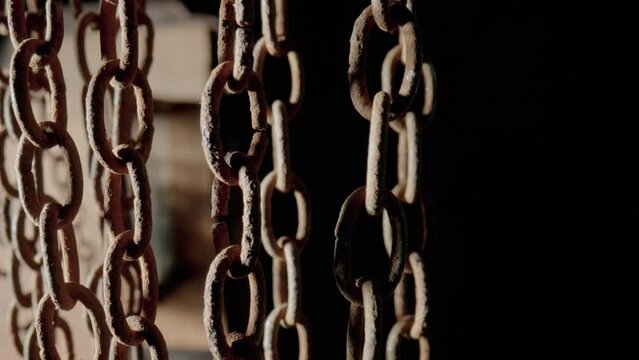 Rusty metal old chain dangling in dark indoor space. Close up of the links of an aged iron chain covered with corrosion and dust. Rough damaged metal structure. Grunge. Strong uneven metal connections