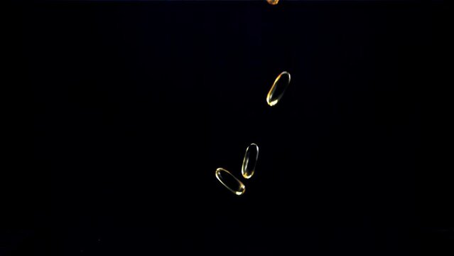 Capsules of vitamin omega 3 fall on the table. On a black background. Filmed on a high-speed camera at 1000 fps.