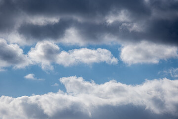 a cloudy blue summer sky with a band of dark clouds above and light clouds below