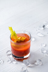 bloody mary cocktail on a white table with red hot chili peppers, celery stick