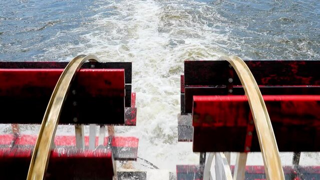 Closeup of the red rotating paddle wheels of a cruise boat in motion on the water, with tilt up to view of La Crosse, Wisconsin, in handleld clip.