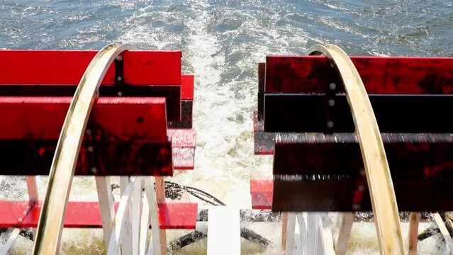 Closeup of the red rotating paddle wheels of a cruise boat in motion on the water, in handleld clip.