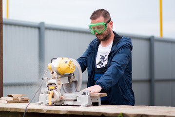 The man works with trimming saw. He is wearing a welder's protective mask and protective gloves. A...