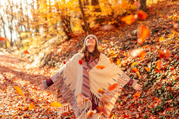 Woman walking through forest watching autumn leaves fall