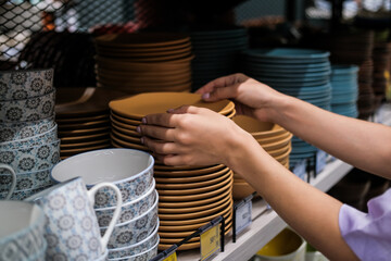 Close up of woman hands choosing ceramic plates in modern tableware shop. Home decor and comfort...