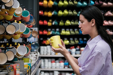 Young woman customer choosing ceramic cups in modern tableware shop. Home decor and comfort concept