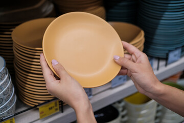 Fototapeta na wymiar Close up of woman hands choosing ceramic plates in modern tableware shop. Home decor and comfort concept