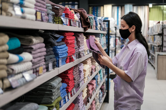 Young woman customer shopping at textile department and choosing towels at home goods store. Home decor and comfort concept