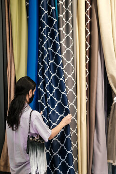 Young woman choosing fabric for curtains in a store. Samples of the curtain hanging on a display rail. Colorful textures of fabric, tulle and furniture upholstery.