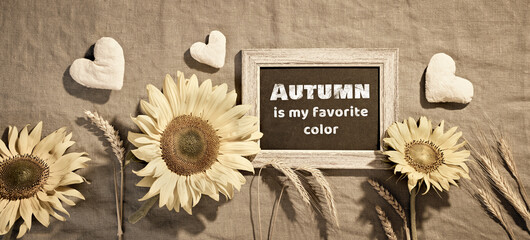 Blackboard with sunflowers and Autumn decorations. Autumn is my favorite color text. Flat lay, panoramic banner on beige textile. Simple, minimal Fall decor. Wheat ears, stuffed cotton hearts.