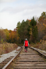 Girl in red vest waling along railway tracks in autumn.