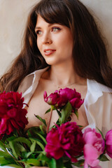 a beautiful young brunette woman in a white shirt with a bouquet of peonies.