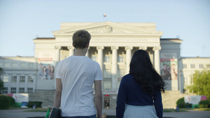 Rear view portrait of two students carrying walking and look at the building. Graphics, formula. Back view of a couple of students sightseeing in a travel destination with a university with colorful