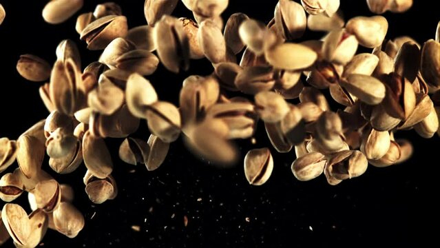 A pile of pistachios rises up and falls. On a black background. Filmed is slow motion 1000 fps.