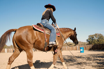 Barrel racing practice shows western cowgirl horseback riding in outdoor arena.