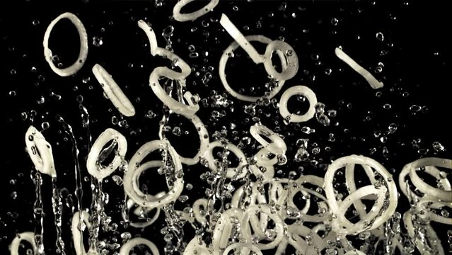 A pile of sliced onion rings with drops of water soars up and falls down. On a black background. Filmed on a high-speed camera at 1000 fps.