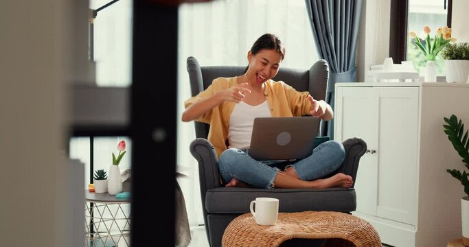 Young asia female girl or university student sit on sofa chair with laptop feel happy enjoy dance done her job, finish work report in living room at home. Work from home, Work life balance concept.