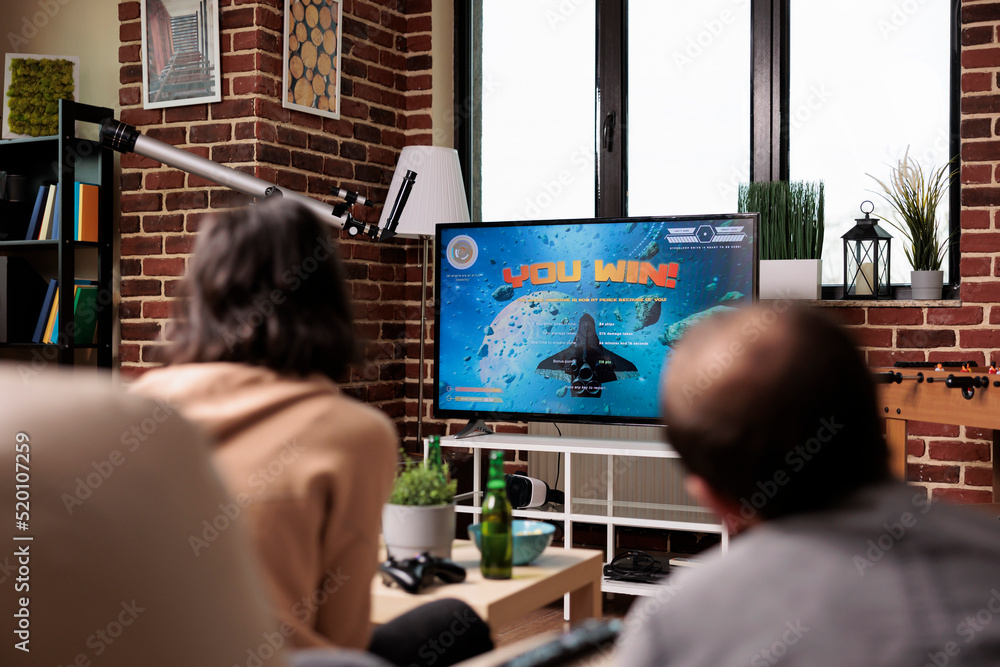 Poster playful multiethnic group of friends sitting on sofa while playing console videogames with controlle