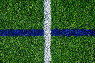 Closeup of artificial grass turf on a recreational sports field, with crossed blue and white stripes, as a graphic background
