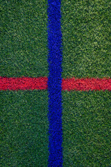 Closeup of artificial grass turf on a recreational sports field, with crossed blue and red stripes, as a graphic background
