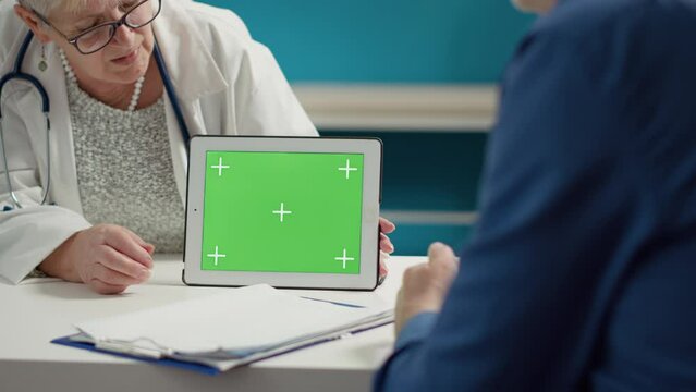 Health specialist holding horizontal greenscreen on digital tablet, at checkup with patient. Mockup blank template with isolated chroma key background and copyspace on display. Close up.