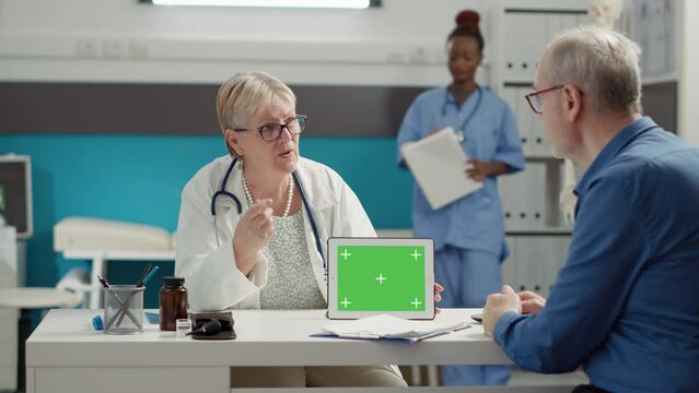 General practitioner analyzing horizontal greenscreen on digital tablet with retired patient in cabinet. Blank mockup template with isolated chroma key and copyspace background on gadget.