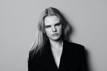 Serious confident sexy fashionable professional female model looks at camera leaning on the studio wall. Black and White shoot concept