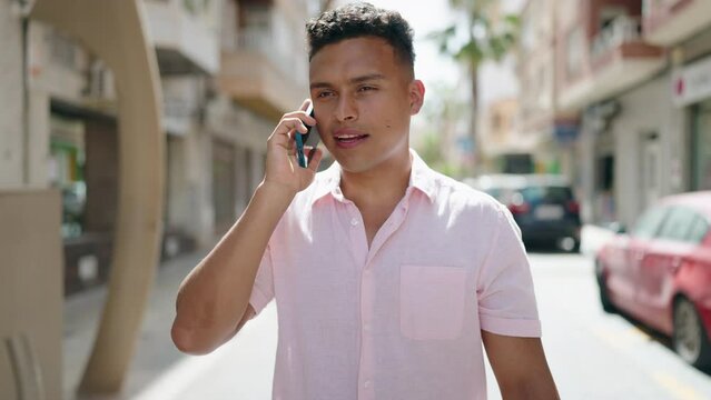 Young latin man smiling confident talking on the smartphone walking at street