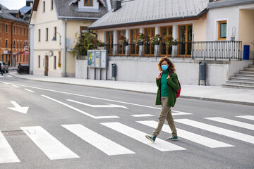 Fototapeta premium Adult Woman Wearing Face Mask Alone Crossing a Pedestrian Crossing in Town Center