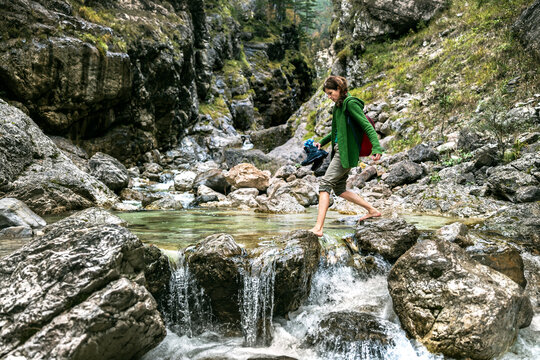 Barefoot Passing Over a Water Stream in Mountain Range Environment for an Adult Woman Backpacker