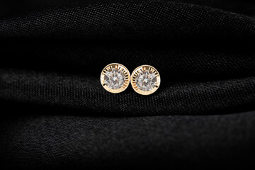 Round golden stud earrings with diamond on black fabric background.