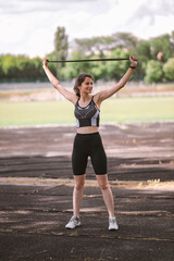 Caucasian beautiful girl athlete in dressed in sportswear with fitness tracker stretching and doing warm up exercise on city stadium in summer. Happy female outdoor sport and healthy lifestyle concept