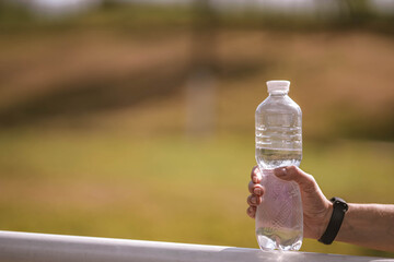 Beautiful Caucasian girl athlete with fitness tracker holds plastic water bottle in her hand on...
