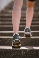 Closeup photo of athlete girl's legs dressed in sportswear with sneakers going up stairs outside in city abandoned stadium . Happy young female sport, travelling, ecology, healthy lifestyle concept
