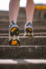 Closeup photo of athlete girl's legs dressed in sportswear with sneakers going up stairs outside in city abandoned stadium . Happy young female sport, travelling, ecology, healthy lifestyle concept