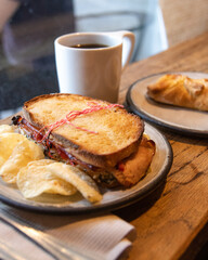 a close-up of a sandwich with chips, coffee, and a pastry. 