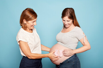 Pregnancy concept. Mother and daughter holding baby socks on pregnant belly