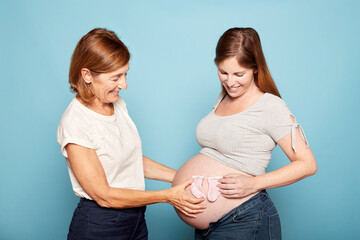 Expecting mother and grandmother holding baby socks on a pregnant belly. Pregnancy concept, family...