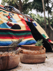 Ceramic jar with medicinal plants infusion in front of traditional Maya sauna covered with Mexican colorful carpets in the tropical forest of Tulum during sacred ceremony