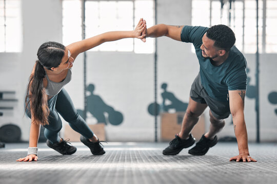 Healthy, fit and active gym partners exercising together as a couple, doing pushups and a high five. Boyfriend and girlfriend training and exercising in a health club as part of their workout routine