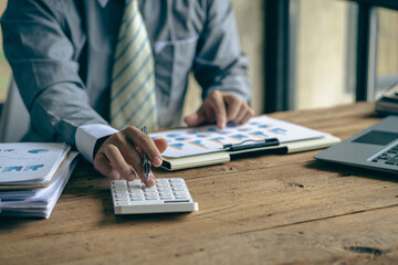 A businessman presses a white calculator to calculate numbers in company financial documents. The finance department prepares accounting documents, analyzing income and expenses in the business.